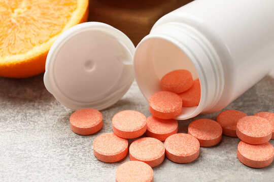 Dietary supplements. Overturned bottle, pills and orange on grey table, closeup
