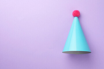 One light blue party hat with pompom on purple background, top view. Space for text