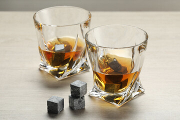 Whiskey stones and drink in glasses on light wooden table, closeup