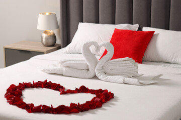 Honeymoon. Swans made with towels and heart of beautiful rose petals on bed in room