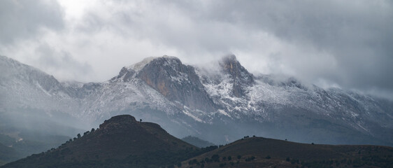 Panoramic view of snow-capped Sierra Arana (2027 meters altitude), southern Andalusia, on a stormy February morning - obrazy, fototapety, plakaty