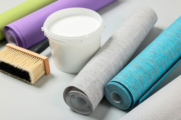 Different wallpaper rolls, brush and bucket with glue on light background