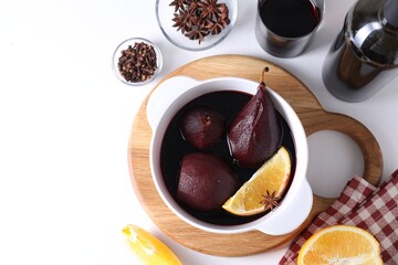 Tasty red wine poached pears in pot, orange and spices on white table, flat lay. Space for text