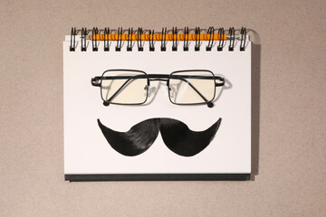 Flat lay composition with artificial moustache and glasses on light brown background