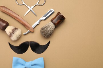 Artificial moustache and barber tools on beige background, flat lay. Space for text