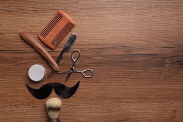 Artificial moustache and barber tools on wooden table, flat lay. Space for text