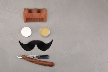 Artificial moustache and barber tools on grey table, flat lay. Space for text