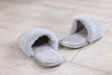 Grey soft slippers on light wooden floor at home, closeup