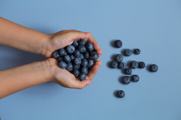 kid's hands with vitamin blueberries on the blue background, top view