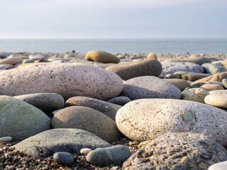 Gray sand and stones close-up on the beach. Stone in the foreground. Beach in winter. Sea coast soil.