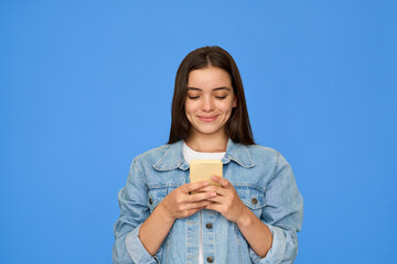 Happy pretty gen z Latin teen girl, smiling teenage student with brunette hair wearing denim jacket holding smartphone, using cellphone looking at mobile phone standing isolated on blue background. - 759136788