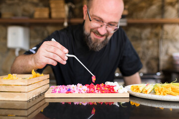 Smiling chef decorating dish with comestible flowers