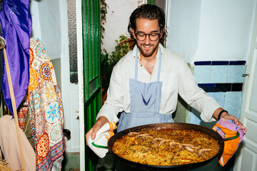 Cheerful man carrying pan with paella at home