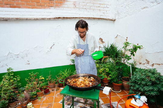 Focused adult man in apron cooking paella on pan