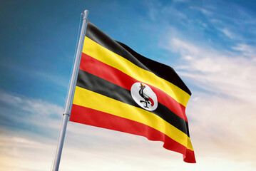 Waving flag of Uganda in blue sky. Uganda flag for independence day. The symbol of the state on wavy fabric.