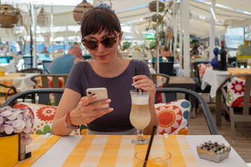 Woman drinking latte and using mobile phone in restaurant