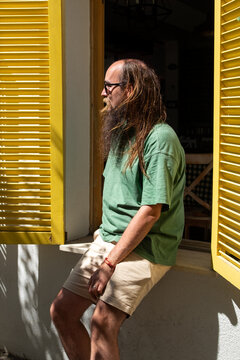 Bearded man with glasses lean on a yellow window a sunny day