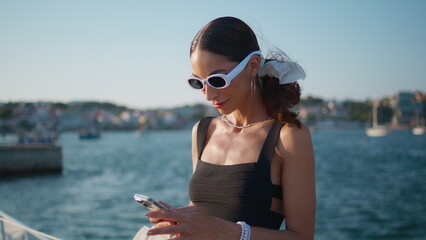 Charming girl looking smartphone screen at sunny seaside close up. Happy woman