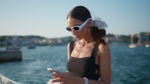 Charming girl looking smartphone screen at sunny seaside close up. Happy woman - Powered by Adobe