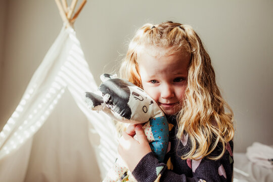 Girls cuddles a cloth doll in against face.