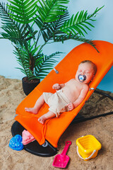 A small newborn boy is sitting in a baby chair. Children's chair chaise longue.