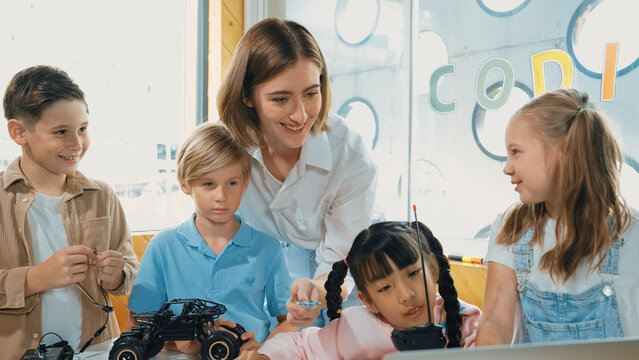 Smart teacher and diverse student looking at laptop on table with car model placed. Caucasian mentor inspect, explain, teaching engineering code or prompt in STEM technology classroom. Erudition.