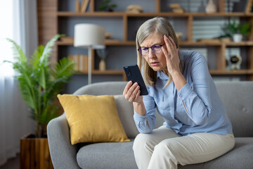 An elderly woman sits on a couch, expressing confusion while looking at her smartphone, possibly...