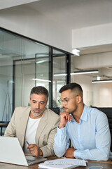 Obraz premium Busy business men executive team working using laptop in office managing data. Two professional businessmen talking, manager consulting client talking about investing finances sit at desk. Vertical