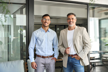 Obraz premium Portrait of two elegant happy confident business men professional executive people partners work team, male company managers looking at camera standing together in corporate office.
