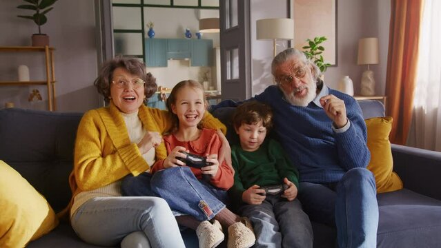 Happy pensioners cheering for grandkids playing on gamepad