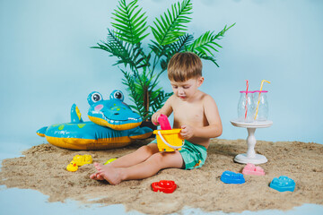 Summer photo zone for children. A little boy in shorts sits on the sand and plays with toys. Summer vacation.
