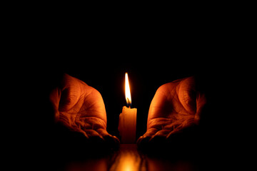 Women's hands near a candle flame in the dark, faith and religion