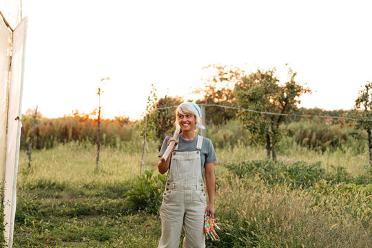 Smiling woman in garden, holding hoe on her shoulder 
