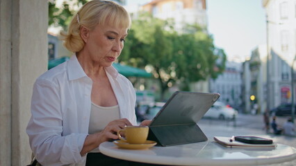 Retired businesswoman working remotely on tablet at city restaurant close up.