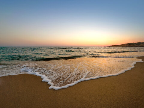 Sandy beach at sunset and sea wave foam