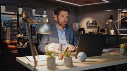 Fototapeta premium Business man drinking coffee late evening workplace closeup. Workaholic typing