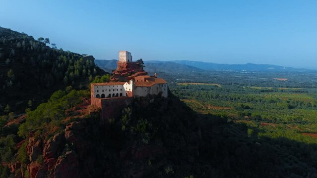 Historical building on hilltop, embraced by trees in natural landscape. Aerial view of medieval castle or manastery on top of mountain and countryside valley below