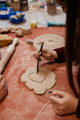 Hand of a person cut out drawing heart on molding from clay at a master class in a pottery workshop