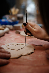 Hand of a person cut out drawing heart on molding from clay at a master class in a pottery workshop