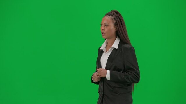 Female reporter isolated on chroma key green screen background. African American woman news host presenter in suit walking and talking. Half-turn.