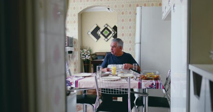 Older 70s male caucasian person at home lunch mealtime in humble residence in South America. candid authentic senior person