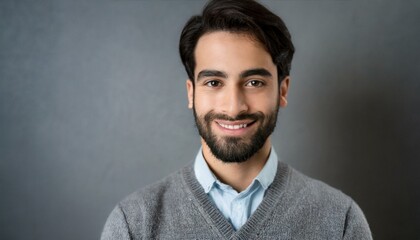 Obraz premium smiling person with a beard, wearing a collared shirt under a v-neck sweater, against a neutral gray background