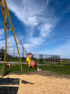 Toddler Boy Rides on Swing at Playground