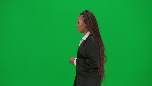 Female reporter isolated on chroma key green screen background. African American woman news host presenter in suit walking and talking. Side view.