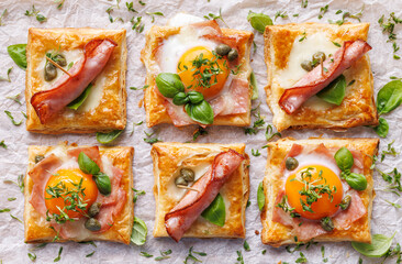 Puff pastry egg and ham mini tarts on a white  background, top view. Delicious breakfast or Easter snack - 759177954