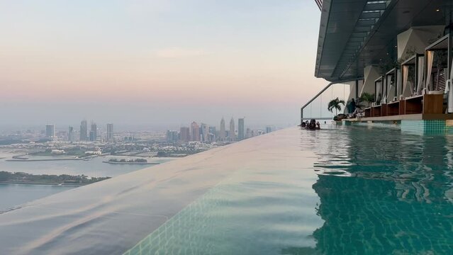 Aerial view of Dubai Palm Jumeirah island, United Arab Emirates. Tourists relaxing in AURA sky pool bar, the world's highest 360 degree infinity pool on Palm Jumeirah overlooking Dubai Marina skyline