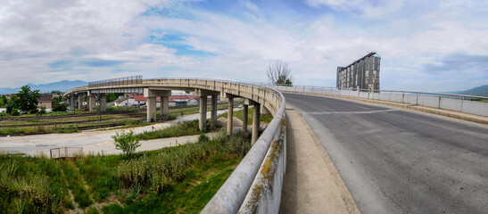 An overpass (bridge) built of concrete pillars and asphalt passes over the track through which the...