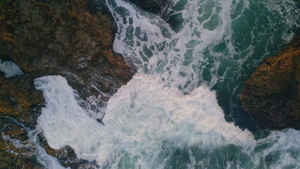 Powerful ocean crashing rocks top view. Beautiful turquoise waves hitting cliffs