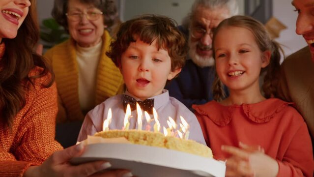 Kid covering face with palms and blowing all candles on cake