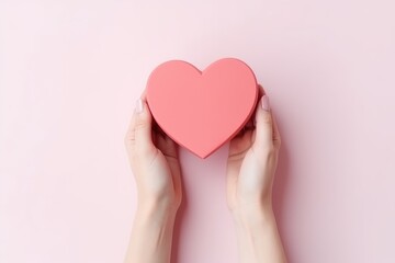 Hands holding a heart-shaped gift box on a pink background. - obrazy, fototapety, plakaty
